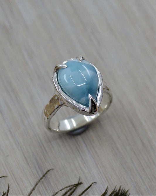 A sterling silver ring with a central Larimar stone, featuring a molten-like effect on the band, placed on a wooden surface.