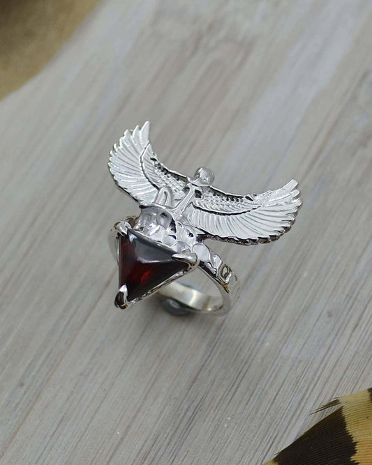 A sterling silver ring with a triangle-shaped garnet at the center, featuring a goddess woman figure with wings extended on top.