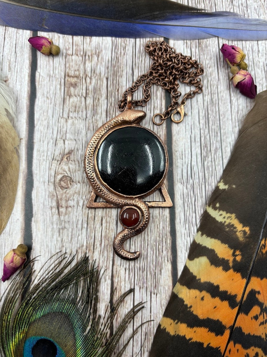 round black tourmaline and small carnelian underneath it with a snake swirling around both joining them together, electroformed