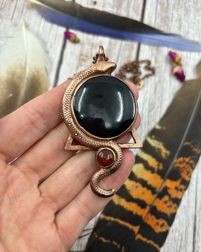 round black tourmaline and small carnelian underneath it with a snake swirling around both joining them together, electroformed