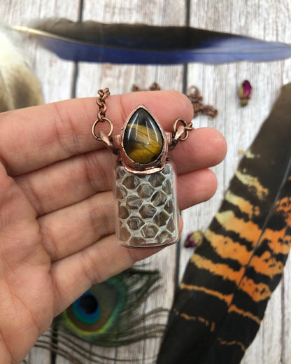 real snake skin in a glass bottle with a tiger eye and copper attached creating a pendant